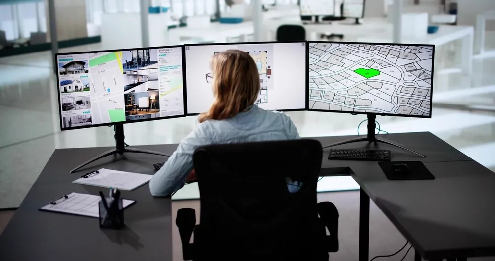 Una agente inmobiliaria haciendo análisis de factibilidad usando tres monitores
